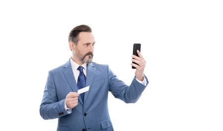 serious mature boss in suit hold credit card and phone isolated on white, selfieの写真素材