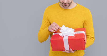 Unshaven man cropped view untie bow on present box grey background copy space, gift