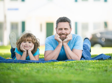 Happy son child and father man enjoy relaxing on blanket on grass summer outdoors, family leisureの写真素材