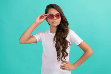 serious teen girl long curly hair in sunglasses casual style on blue background, summer styleの写真素材
