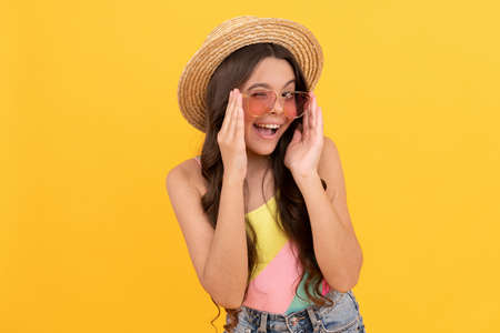 amazed child in summer straw hat and glasses has curly hair on yellow background, beach fashionの写真素材