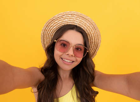 happy kid in summer straw hat and glasses making selfie on yellow background, summer selfieの写真素材