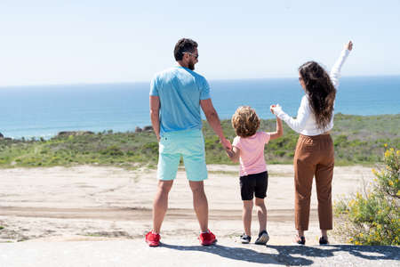 family of mom dad and child boy looking in future holding hands in summer, back view, happy familyの写真素材