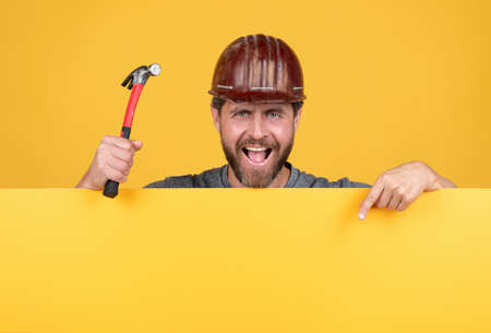 happy labour day. mature man in helmet with hammer. builder point finger on copy spaceの写真素材