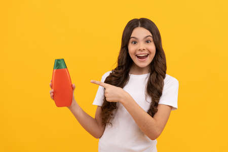 amazed teen girl with long hair pointing finger on shampoo bottle, promotionの写真素材