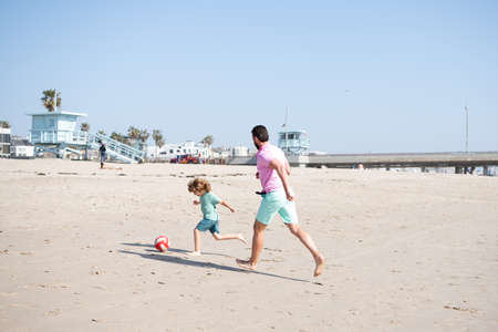 happy father and son playing football having fun on summer sandy beach family vacation, parentingの写真素材