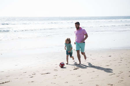 sport activity. father and son play soccer or football on beach. daddy with kid boy on summer dayの写真素材