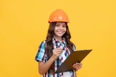 happy teen girl in construction helmet making notes in clipboard, making notesの写真素材