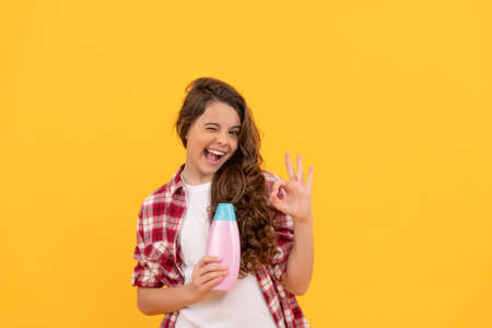 happy teen girl with long curly hair hold shampoo bottle, advertの写真素材