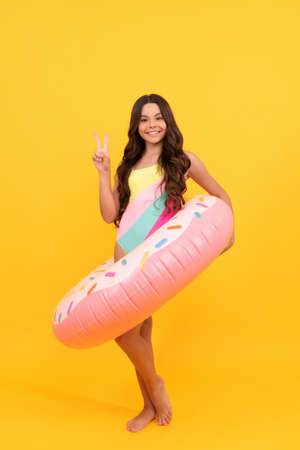 happy beach child in swimsuit with doughnut inflatable ring on yellow background, summer.の写真素材