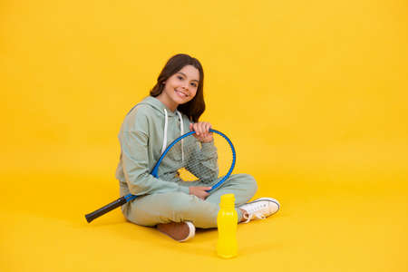 happy child sit with tennis racket and water bottle on yellow background, healthy lifestyle.の写真素材