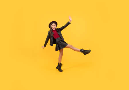 happy teen girl in hat and leather clothes making wide step forward, carefreeの写真素材
