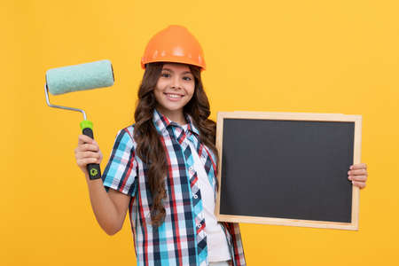 happy child with curly hair in helmet hold paint roller and school blackboard copy space, renovationの写真素材