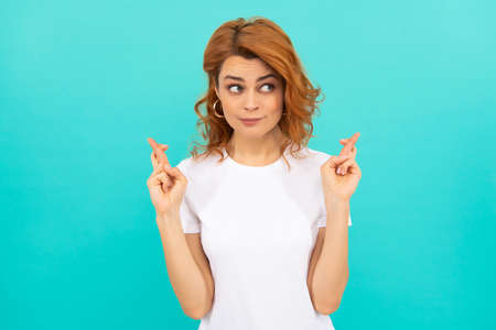 dreamy redhead girl with curly hair cross fingers making a wish on blue background, dreamの写真素材