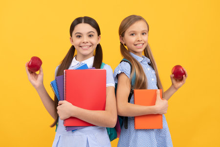 Happy pupils with books hold vitamin organic apples yellow background, school breakfastの写真素材