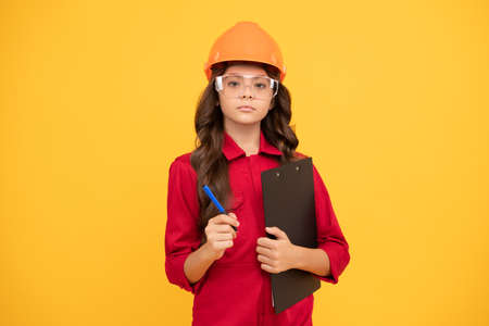 serious child girl in protective hard hat and glasses hold folder with paper documents, examiningの写真素材