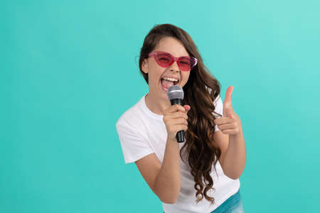 Happy girl singer point finger gun singing song to microphone blue background, karaokeの写真素材