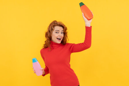 happy redhead lady curly dyed hair choosing body care product of shampoo having fun, beauty product.の写真素材
