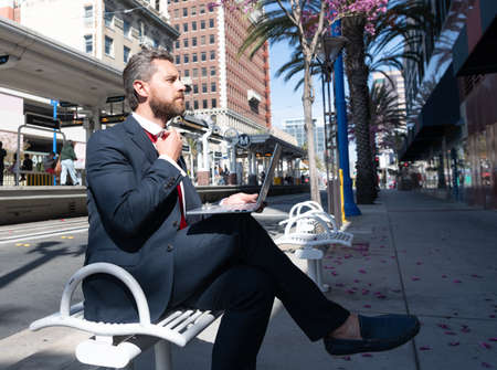 mature man businessman sit on bench in outdoor city working online on laptop, business success.の写真素材