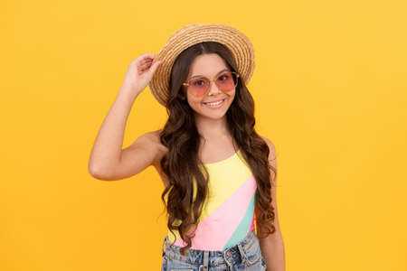 happy teen girl in summer straw hat and glasses has curly hair on yellow background, fashionの写真素材