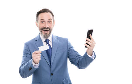 happy mature office manager in suit hold debit card and smartphone isolated on white, internet buyの写真素材