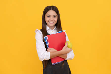 Happy schoolchild in uniform hold apple and books yellow background, back to schoolの写真素材