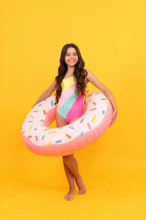 happy teen girl in swimming suit with doughnut inflatable ring on yellow background, summertime.の写真素材