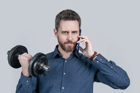 serious strong bearded man businessman training with barbell and talking on phone, communicationの写真素材