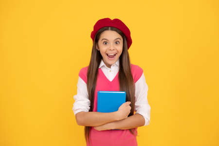 surprised teen school girl in french beret hold copybook on yellow background, schoolの写真素材