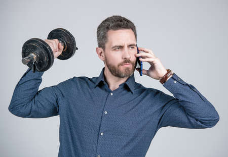 strong bearded man businessman training with barbell and speaking on smartphone, helloの写真素材