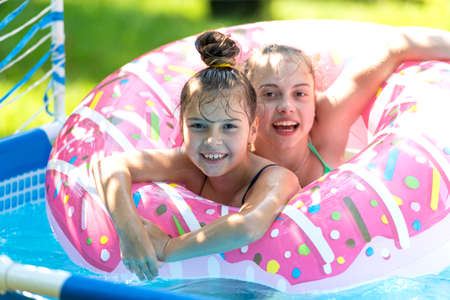 The perfect way to stay cool. Happy kids swim in donut pool float. Pool games. Poolside play. Summerの写真素材