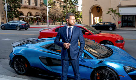handsome man real estate agent in formal suit standing near luxury automobile, car insuranceの写真素材