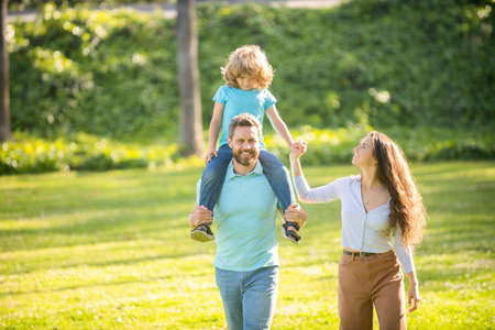 Happy family of mother and father carrying boy child on shoulders summer outdoors, parentsの写真素材