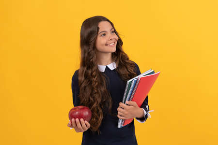 smiling teen girl hold school copybooks and apple lunch on yellow background, back to school.の写真素材
