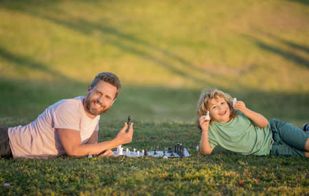 dad and kid play logic game. father and son playing chess on grass in park. fathers day.の写真素材