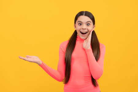 surprised child presenting product on copy space on yellow background, big saleの写真素材