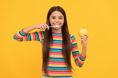 Happy girl child brush teeth with toothbrush holding apple yellow background, healthy teethの写真素材
