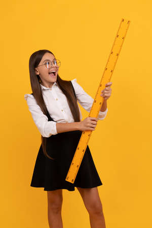 surprised nerd teen girl in uniform and glasses hold mathematics ruler for measuring, back to schoolの写真素材