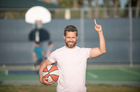 happy muscular man sportsman basketball player raised finger hold ball outdoor, sportの写真素材
