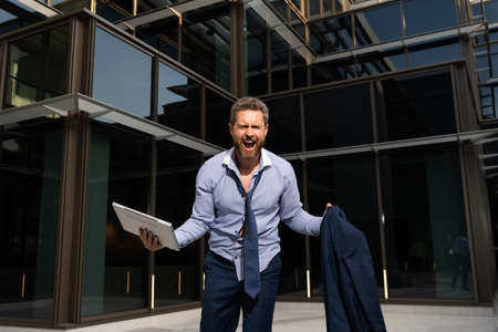 frustrated businessman man shouting in rage with computer and jacket, business collapseの写真素材