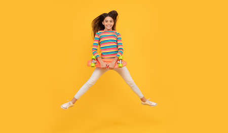 skateboarding. happy child jump with penny board. teen girl on yellow background.の写真素材