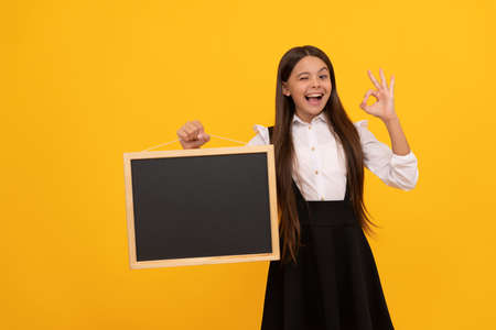 surprised child in uniform hold school blackboard for copy space showing ok gesture, advertisingの写真素材