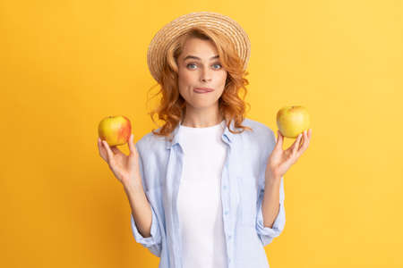 cheerful young woman in summer straw hat with apple licking lips, yummy.の写真素材