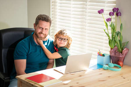 happy dad helping his school son child in glasses study with computer at home, education.の写真素材