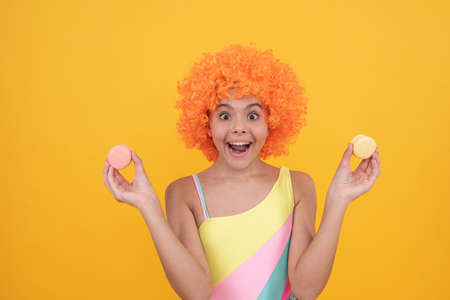 sweet tooth. funny kid in clown wig hold french macaron. amazed child wear swimsuit.の写真素材