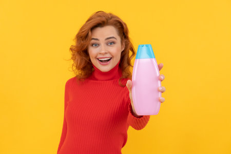 happy redhead woman curly dyed hair presenting body care product of shampoo, beautyの写真素材