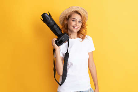 cheerful redhead woman photographer with camera in straw hat making photo, cameramanの写真素材