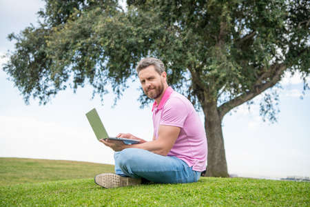 cheerful guy check email on computer relaxing on grass, video conference