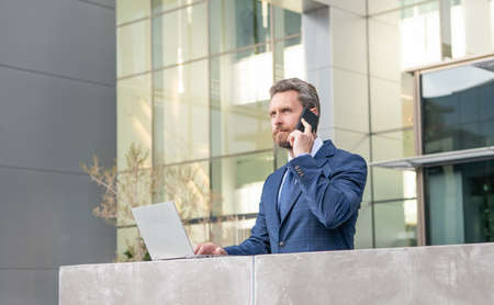 entrepreneur in suit has phone conversation while using pc outside the office, communication.の写真素材