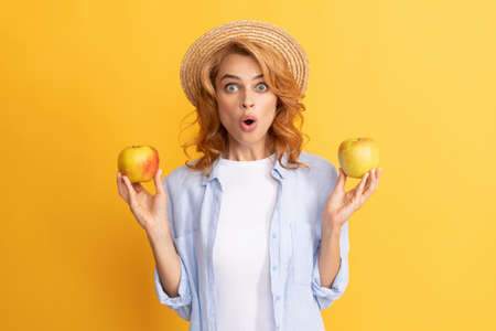 surprised young woman curly hair in summer straw hat with apple, healthy foodの写真素材